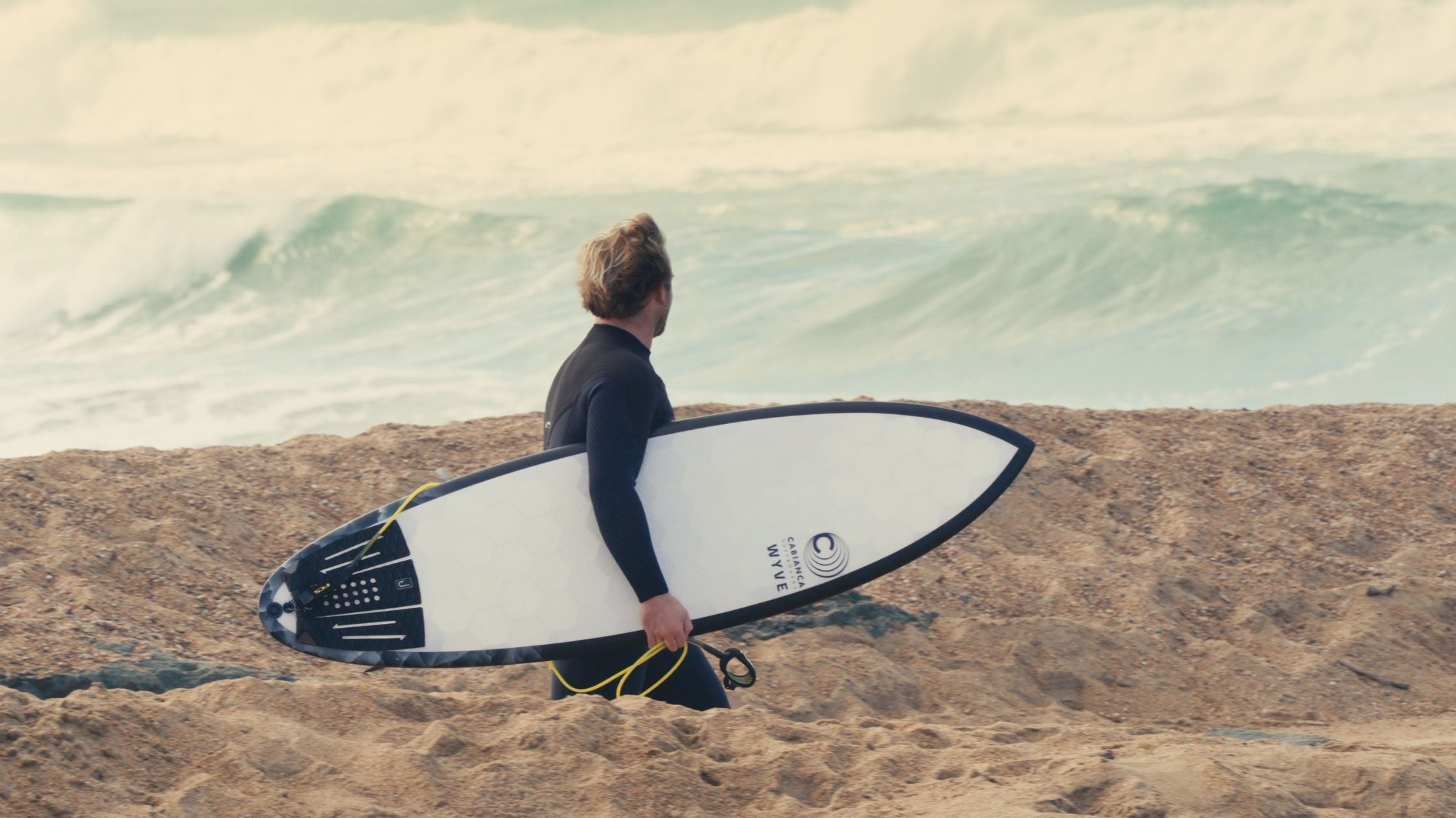 un surfeur avec une planche de surf wyve sous le bras