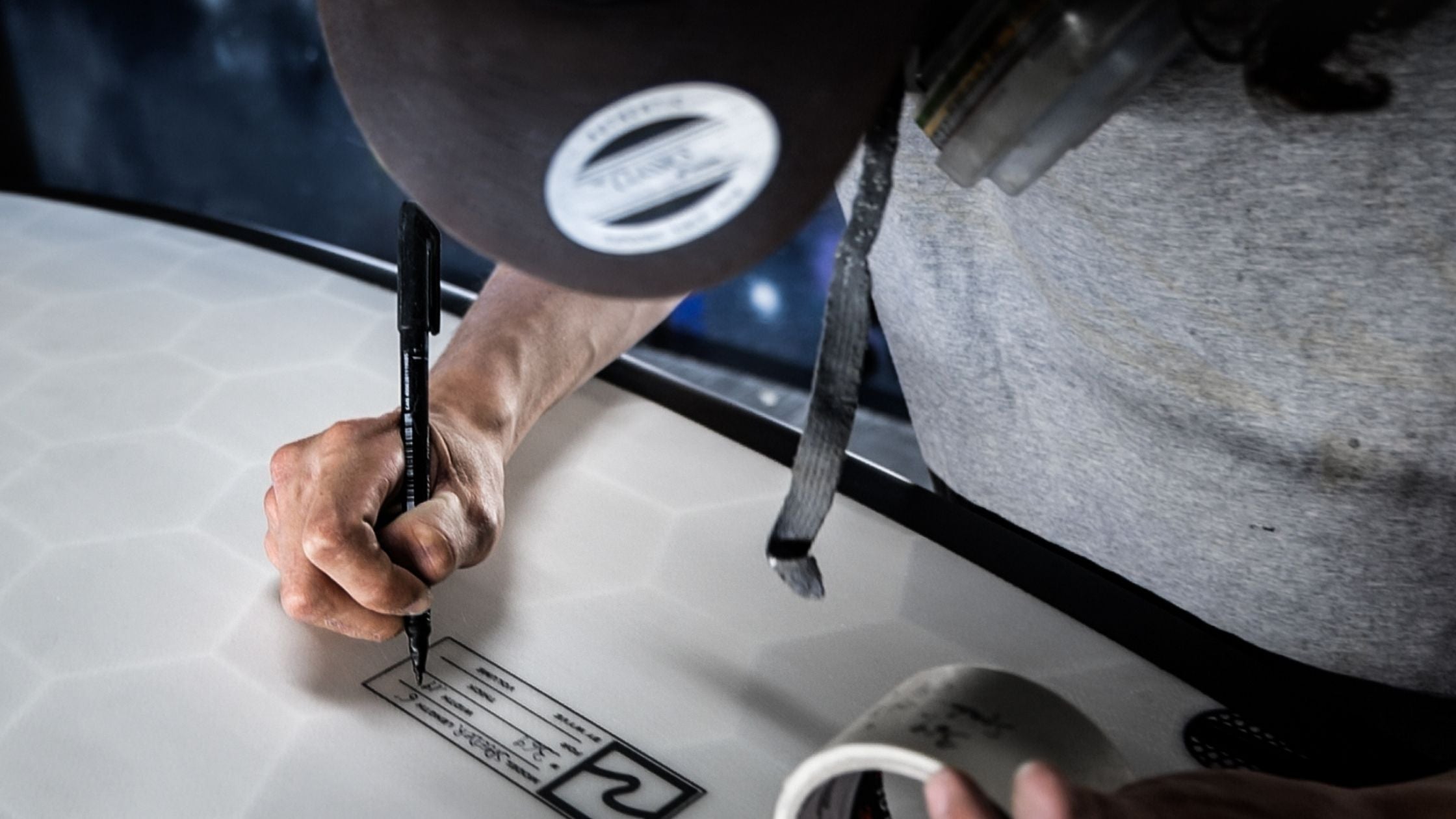 Shaper writing on the bottom of a 3D printed surfboard from Wyve in a surf shaping room