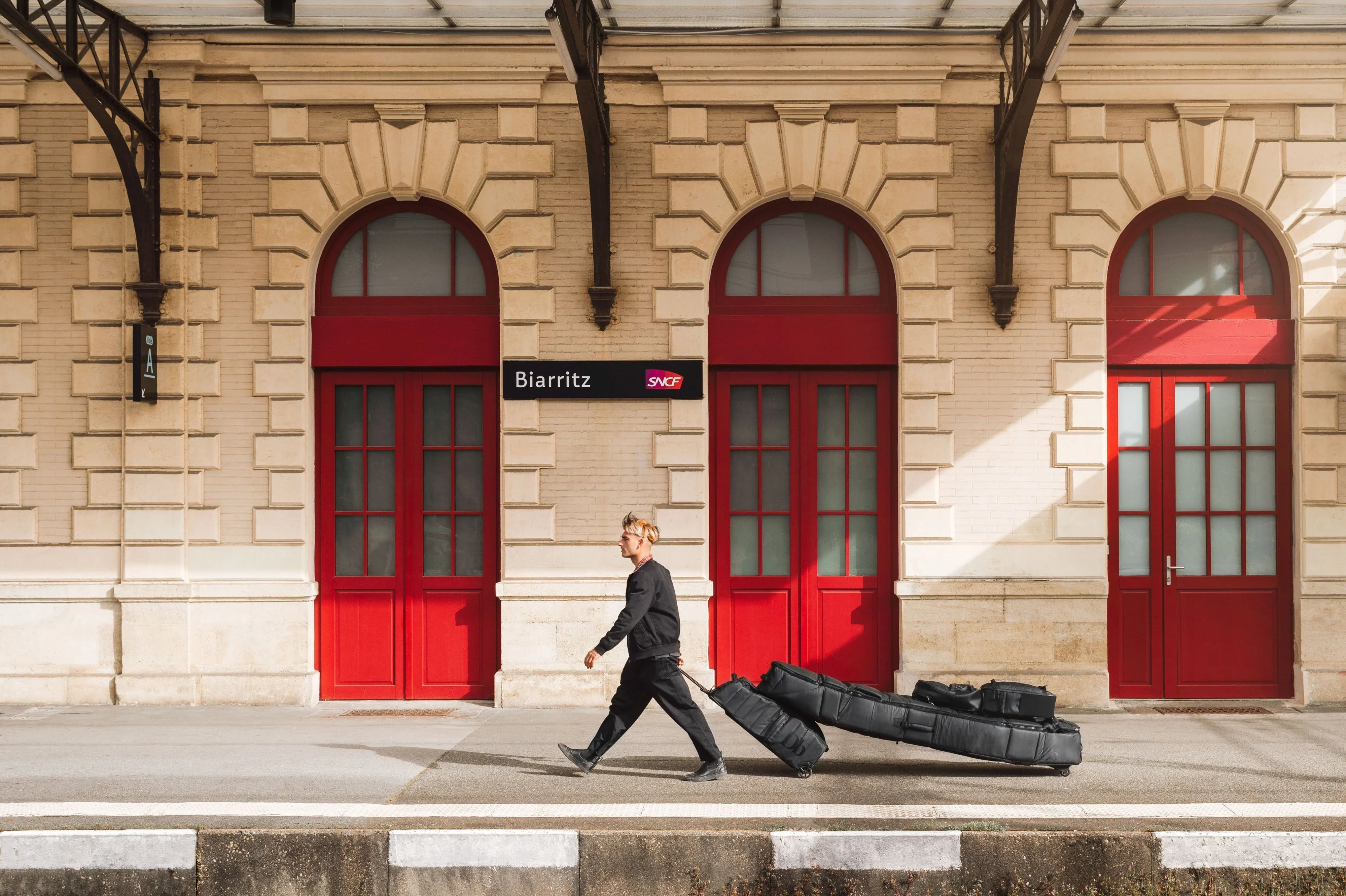 Un surfer en train de transporter une planche de surf devant une gare SNCF